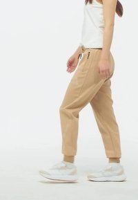 Béžové jogger nohavice s zužujúcimi sa manžetami, sťahovacím pásom a bočnými zipsovými vreckami. Kombinované s bielymi športovými topánkami a priliehavým bielym tričkom.
