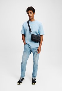 Lys blå tekstureret kortærmet skjorte, parret med slidte blå jeans. Accessory: sort crossbody taske med sølv hardware. Sneakers med sorte og gule accenter.