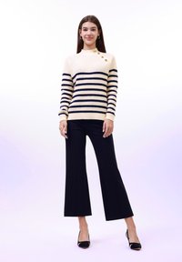 Pull en ivoire avec des rayures marine, des poignets côtelés et trois boutons dorés à l'épaule ; associé à un pantalon large noir et des talons.