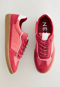 Sneakers rossi con una miscela di texture lisce e scamosciate, accenti bianchi, lacci tondi e suola in gomma. Include dettagli perforati sulla punta.