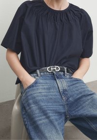 Top blu navy a maniche corte con scollatura arricciata, abbinato a jeans in denim blu sbiadito e una cintura nera con fibbia in argento.