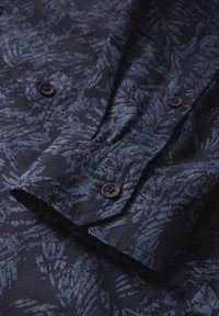 Námornícky košile s texturovanou látkou a vzorem listů v různých odstínech modré. Černé knoflíky na manžetách a légě.