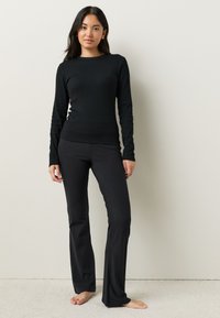 Top negro de manga larga con textura acanalada combinado con pantalones ajustados negros, ambos hechos de un material suave y elástico.