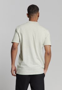 Lichtgroen poloshirt met korte mouwen en een fijne textuur, met een klassieke kraag en een ontspannen pasvorm, gezien vanaf de achterkant.