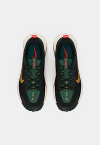 Nike sneakers featuring a black mesh upper, green accents, orange logo, and red heel tab; textured sole for grip.