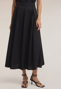 Falda negra hasta la rodilla con pliegues, hecha de una tela suave. Combinada con tacones negros de tiras que muestran un diseño de tacón delgado.
