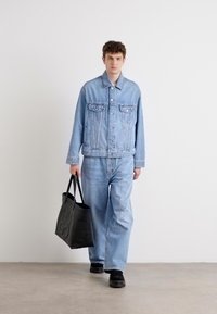 Light blue denim jacket with two front pockets, paired with matching loose-fit jeans. Black tote bag with embossed lettering. Black shoes.