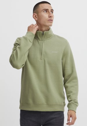 Green fleece pullover with a half-zip collar, featuring a small logo on the chest, ribbed cuffs, and a relaxed fit design.