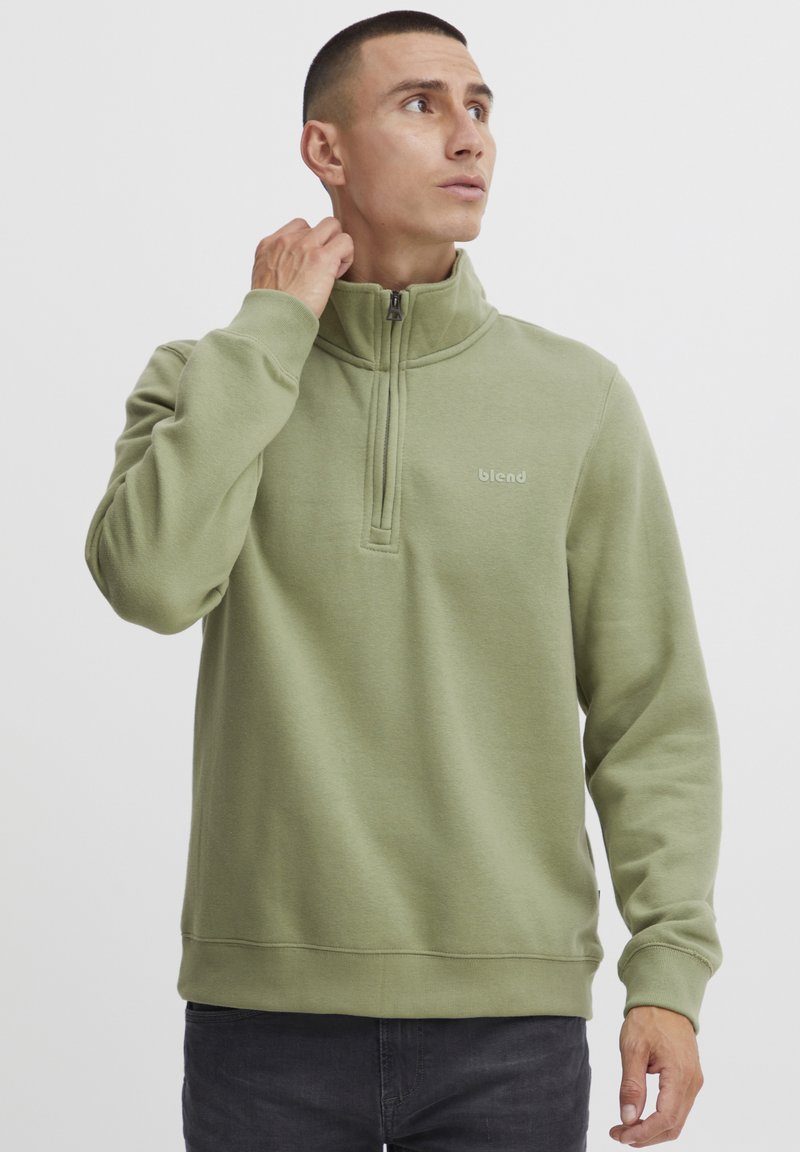 Sudadera de forro polar verde con cuello de media cremallera, que presenta un pequeño logo en el pecho, puños acanalados y un diseño de corte relajado.