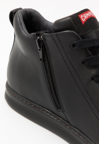 Svart lær høy-topp sneakers med sidelukking, runde snørebånd og en kontrasterende sømt midtsåle. Har en Camper-logo på tungen.