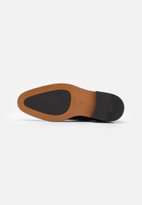 Sole di scarpa in pelle nera con tacco in gomma beige, caratterizzata da una presa nera texturizzata e un logo impresso. Bordo diritto e design minimale.