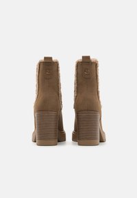 Bottines marron avec un intérieur doux et duveteux, des talons blocs rayés, un extérieur en daim lisse et un détail en languette à l'arrière.