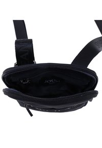 Svart tygaxelväska med dragkedja, som har ett rymligt interiör och en märkesrem. Inuti finns en mjuk foder och ett fack.