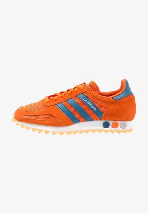 Baskets Adidas L.A. Trainer orange avec des bandes bleues, une semelle blanche et des accents circulaires multicolores sur le côté du talon.