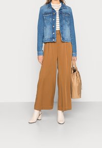 Veste en jean bleu clair ; chemise rayée blanche et marine ; pantalon large couleur fauve ; bottines à talon carré crème ; sac beige.