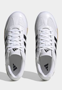 Baskets blanches avec une tige en maille et en cuir, un design à trois bandes noires et des semelles texturées. Les lacets sont blancs ; la marque est visible à l'intérieur.