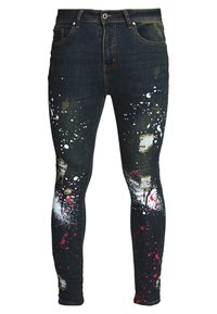 Jeans de mezclilla oscura con un corte ajustado, que presentan salpicaduras de pintura en blanco y rojo, áreas desgastadas y acentos dorados en la tela.