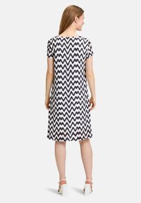 Kurzärmliges Kleid mit einem weißen und dunkelblauen Zickzackmuster, knielang, mit runder Ausschnitt und lockerer Passform. Sanfte Stofftextur.