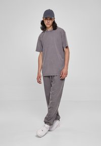 Tricou din bumbac gri cu umeri căzuți, asortat cu pantaloni coordonați. Ambele au un aspect decolorat și o textură moale. Întregul outfit este completat de o caciulă gri.