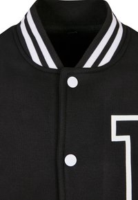 Schwarzer College-Jacke-Kragen mit weißen Streifen und weißen Druckknöpfen, mit einem teilweise weißen Umriss eines Buchstabens auf der Brust.