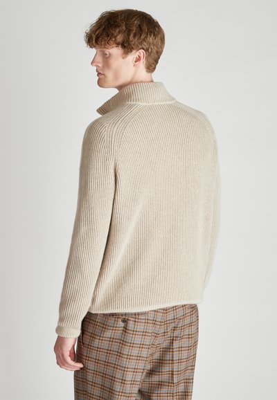 Beige Rippstrickpullover mit hohem Kragen und lässiger Passform, kombiniert mit karierten Hosen in Braun- und Blautönen.