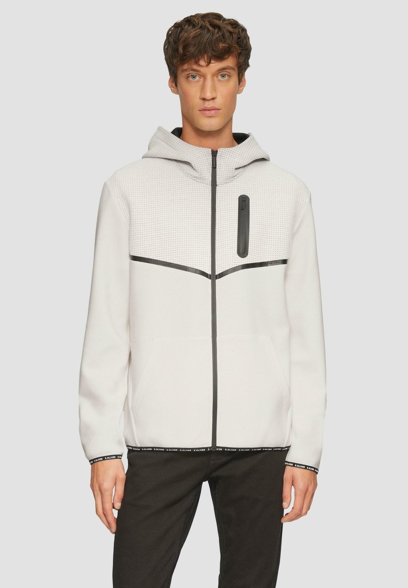 Witte zip-up hoodie met een gestructureerde capuchon, zwarte accenten, voorzakken en een horizontale zwarte streep over de borst.