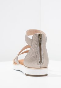 Metaliczne skórzane sandały z tylnym zamkiem błyskawicznym, z paskiem na kostkę i białą, żebrowaną podeszwą, pokazane z tylnego kąta na białym tle.