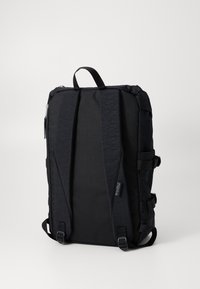 Sac à dos noir en tissu durable avec une forme rectangulaire. Il dispose de bretelles rembourrées et ajustables, d'une poignée supérieure et d'un compartiment zippé.