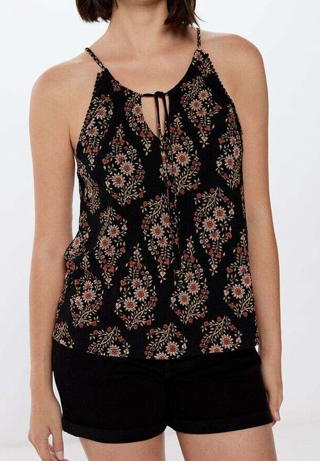Femme portant un haut sans manches noir à motifs floraux avec fines bretelles et un short noir sur un fond uni.