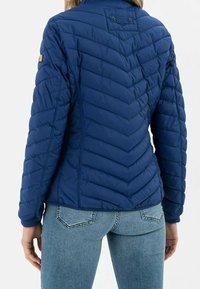 Sinih takki, mukaisesti chevron-muotoilu, jossa on korkea kaulus ja ribbetut hihansuut, suunniteltu lämmön ja mukavuuden takaamiseksi.