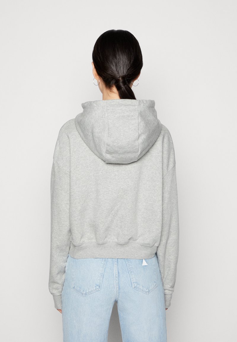 Heather šedá cropped mikina s prostornou kapucí, spadlými rameny, žebrovaným lemem a detailem švu na zádech, v kombinaci se světle modrými džíny.