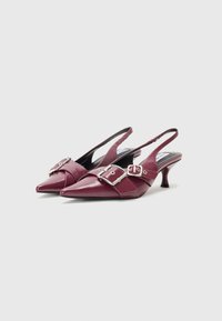 Sandale cu toc slingback din piele patent burgundy, cu vârful ascuțit, având un accent cu cataramă îndrăzneață și un toc subțire, curbat.