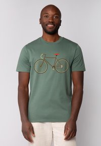 Groene katoenen t-shirt met een fietsafbeelding in bruin en een rode zitting. Korte mouwen en een ronde halsontwerp. Zachte textuur.