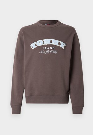 Ruskea svetari puuvillaseoksesta, jossa on valkoinen ja vaaleansininen "TOMMY JEANS" -logo. Ribatut hihansuut ja helma sekä pyöreä kaula-aukko.