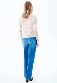 Gestreiftes langärmliges Oberteil in zartem Rosa und Creme, kombiniert mit blauen geraden Jeans. Glatte Textur, einfaches Design und klassischer Schnitt.