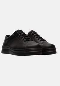 Black leather sneakers with a smooth finish, round toe, thick black rubber sole, and six lace eyelets for secure closure.