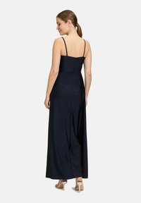 Robe maxi bleu marine avec fines bretelles, corsage ajusté et jupe fluide. Dotée d'une fermeture éclair au dos et d'une texture lisse. Sandales à talons hauts argentées.