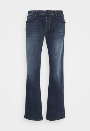 Jean en denim bleu foncé à coupe évasée avec un design à cinq poches, des coutures visibles et une fermeture éclair. Des décolorations le long des cuisses et des hanches sont présentes.