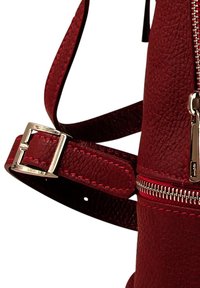 Sangle en cuir rouge texturé réglable avec boucle en argent, attachée à un sac en cuir rouge avec une fermeture éclair en argent.
