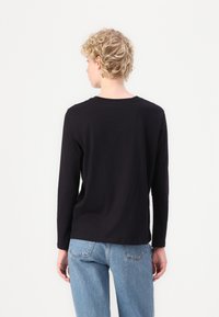 Zwart katoenen shirt met lange mouwen, ronde hals, ontspannen pasvorm en gladde textuur, gecombineerd met lichtblauwe denim jeans.
