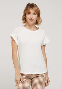 T-shirt blanche à manches courtes avec un col rond et des manches raglan, fabriquée en tissu doux, associée à un pantalon à motifs vichy marron.