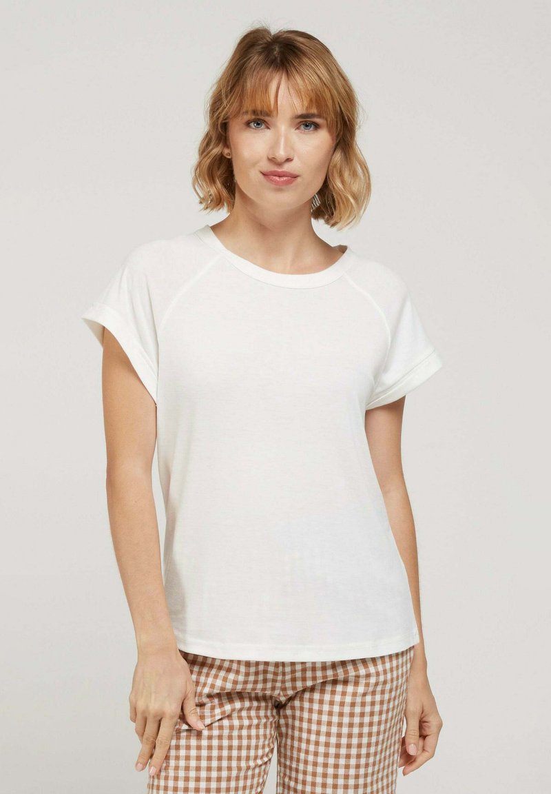T-shirt blanche à manches courtes avec un col rond et des manches raglan, fabriquée en tissu doux, associée à un pantalon à motifs vichy marron.