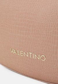 Rosa texturerad läderväska med en guldfärgad "Valentino"-logotyp. Ytan har ett subtilt reptilmönster som förbättrar dess visuella tilltalande.