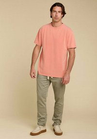 T-shirt à manches courtes de couleur corail rose, assorti à un pantalon vert clair. Le t-shirt a un encolure ronde; le pantalon présente des détails avec cordon de serrage et des jambes fuselées.