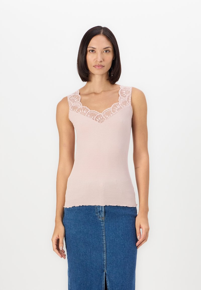 Light pink ribbed tank top with a lace-trimmed v-neckline, scalloped hem, paired with a blue denim skirt featuring a front slit.