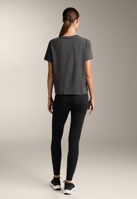 Siva majica s kratkimi rokavi, v kombinaciji s črnimi legicami in črnimi čevlji. Gladek material, prilegajoča se silhueta in minimalisticen dizajn.