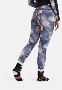 Wielokolorowe legginsy w niebieskie i różowe abstrakcyjne wzory, z wysokim stanem i kontrastowymi detalami szwów; w połączeniu ze wzorzystymi skarpetkami.