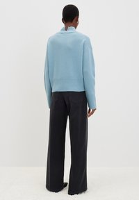 Maglione di colore azzurro chiaro a maglia con collo alto e orlo a costine, abbinato a jeans neri a gamba larga a vita alta. Focus su texture morbide.