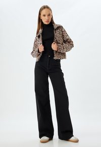 Leopardenmuster Reißverschlussjacke, gerippter schwarzer Rollkragenpullover, hochtaillierte schwarze weite Hosen und bequeme Schuhe mit Gummi-sohlen.