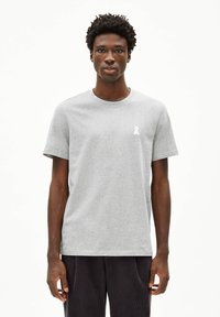 Grijze katoenen T-shirt met een ronde hals en korte mouwen. Heeft een klein wit lintlogo op de linkerborst. Minimalistisch ontwerp.